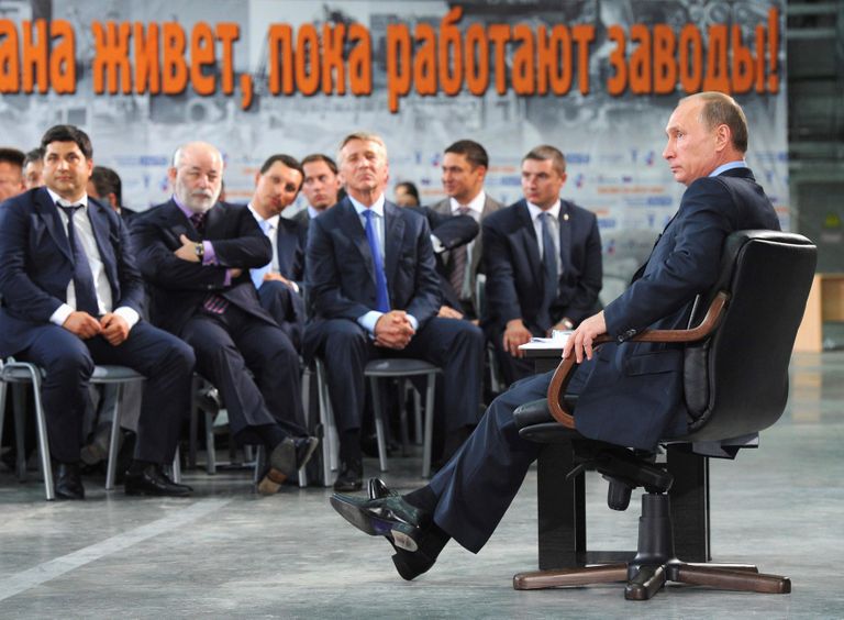 Путин на встрече с бизнесменами в 2013 году. На стене надпись - "страна живет, пока работают заводы".