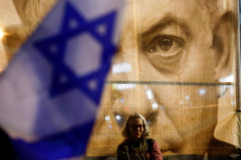 Участница протестов в Израиле на фоне большой фотографии с премьер-министром Биньямином Нетаньяху, Тель-Авив, Израиль, 28 января 2023 года.