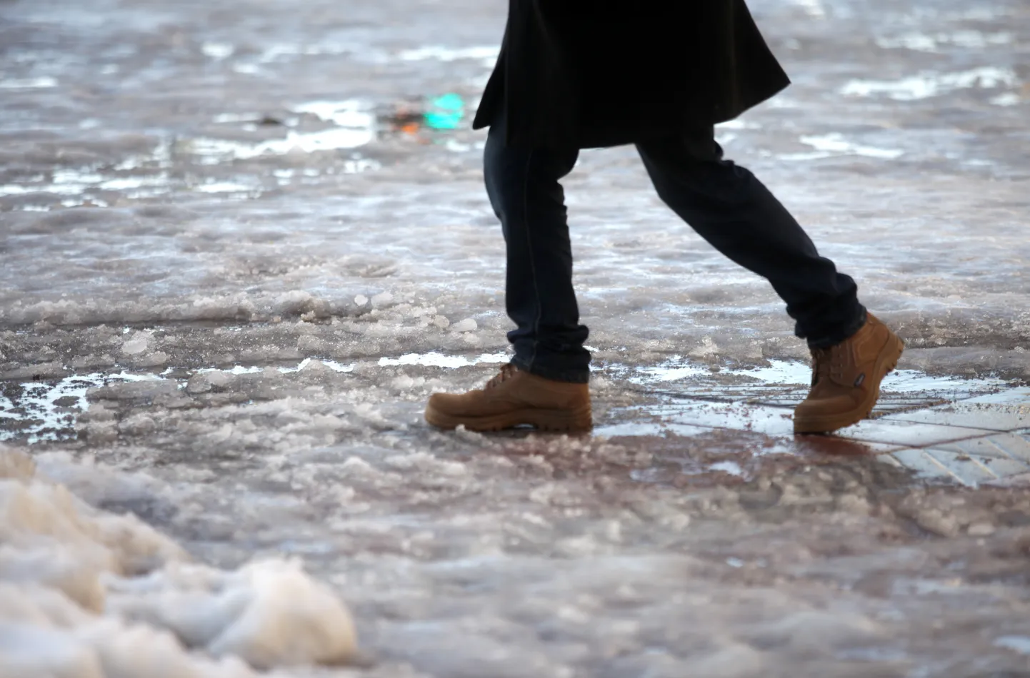 Cilvēka kājas un izkusušais sniegs uz ietves; ilustratīvs foto.