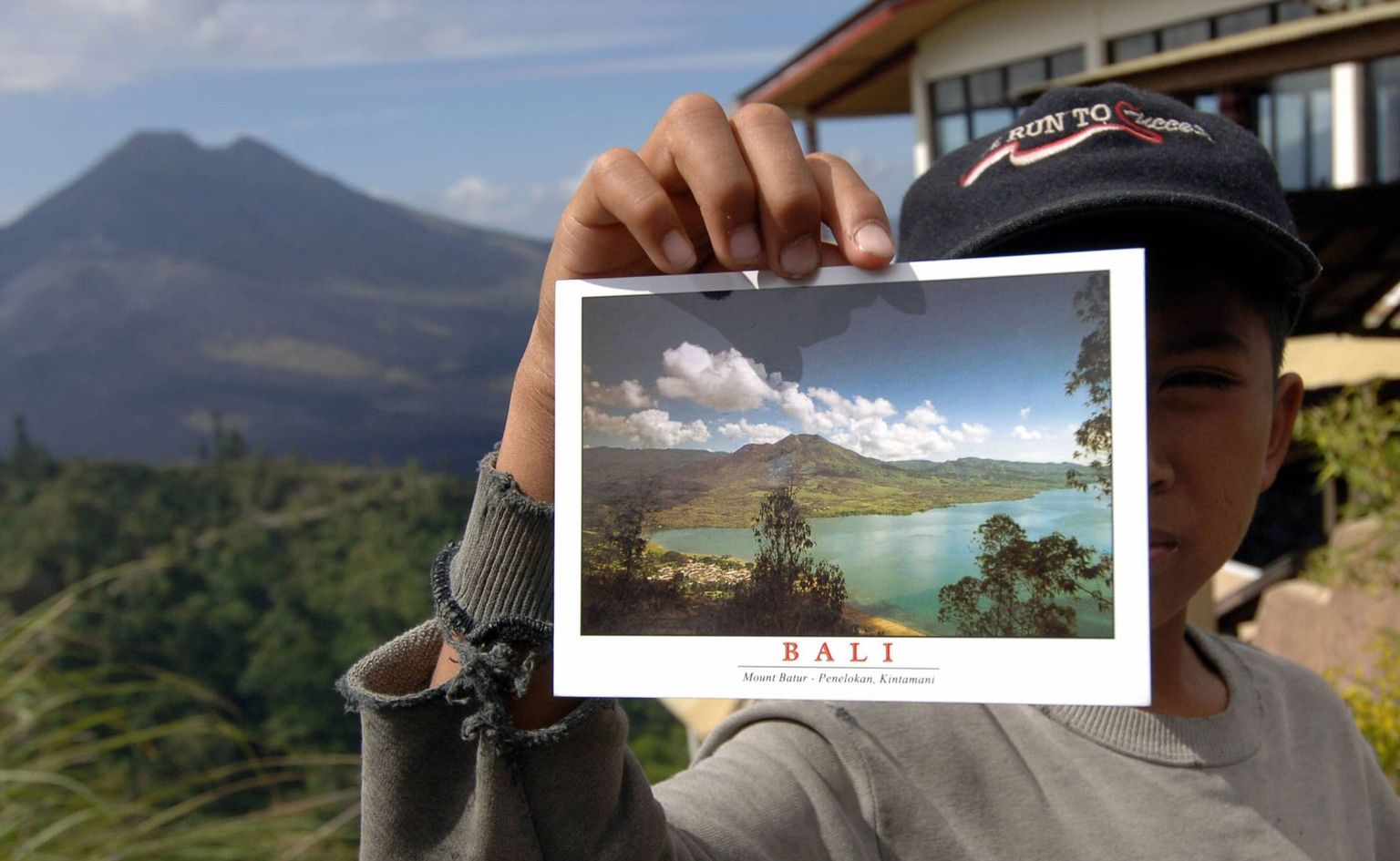 Kaupleja näitab Bali saarel postkaarti. Taamal Baturi vulkaan.