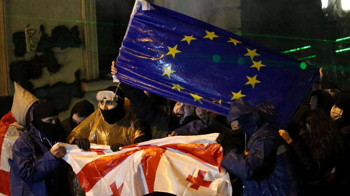 Люди в плащах держат мокрые флаги Грузии и ЕС.