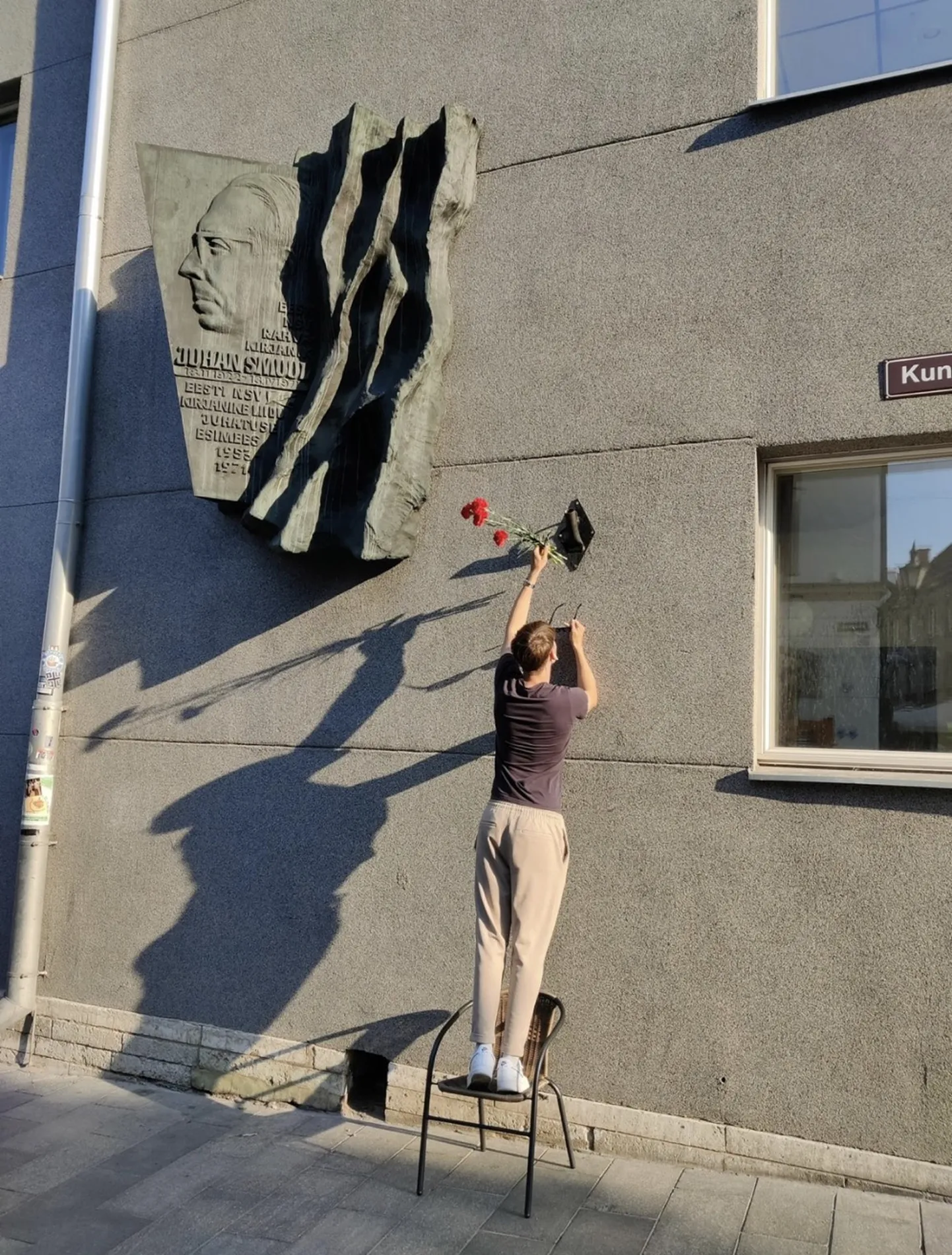Неизвестный возлагает красные гвоздики к барельефу писателя Смуула в центре Таллинна.