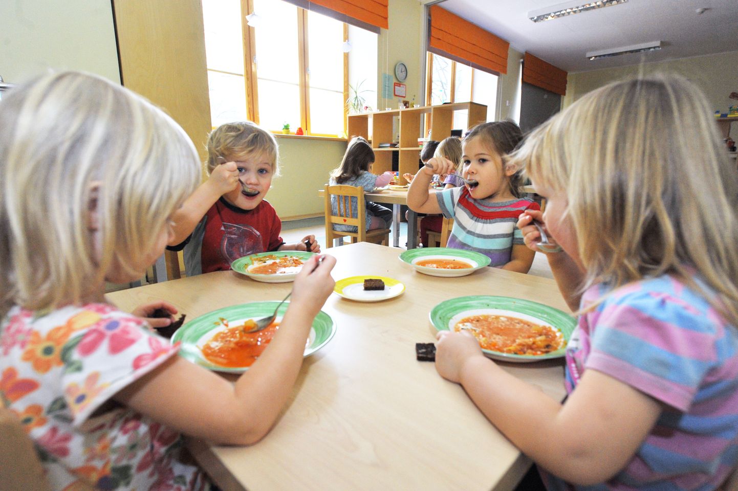 Illustreerival pildil lapsed lasteaias lõunasööki söömas