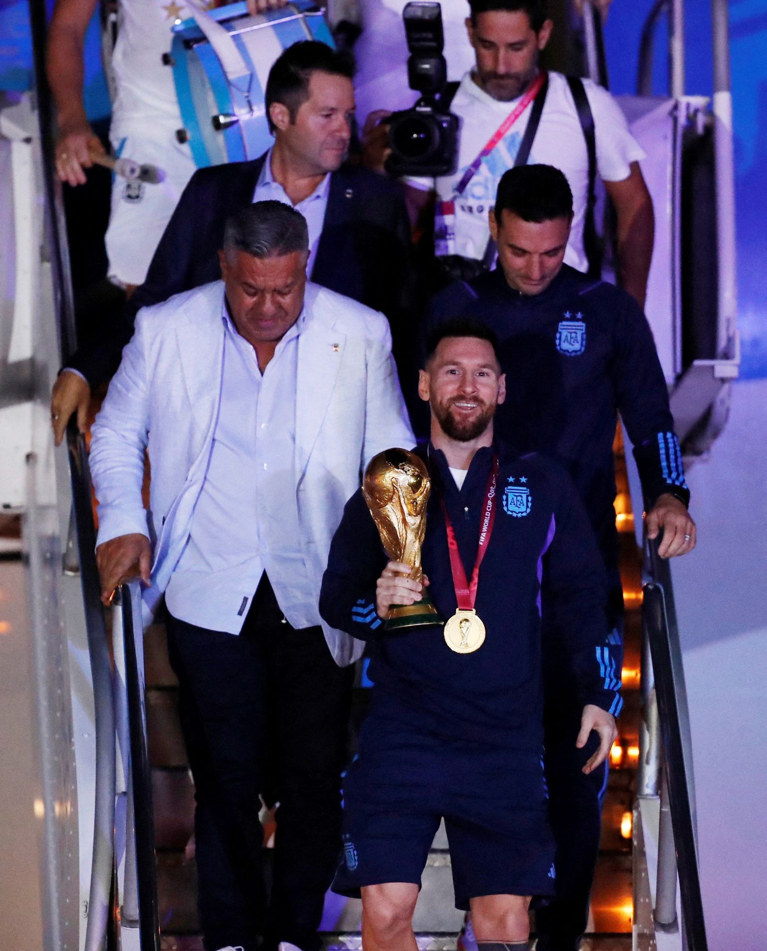 Katari MMi võitnud Argentina jalgpallikoondis jõudis koju tagasi 20. detsembril. Pildil on Lionel Messi, kelle käes on MMi karikas, ta meeskonnakaaslased, ametnikud ja fotograafid astumas Buenos Aireses Ezeiza lennujaamas lennukilt maha