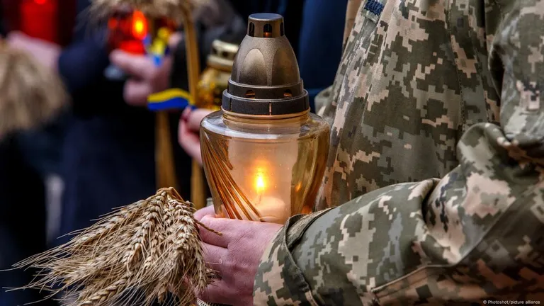Военный держит в руках колосья пшеницы и свечу в память о жертвах Голодомора