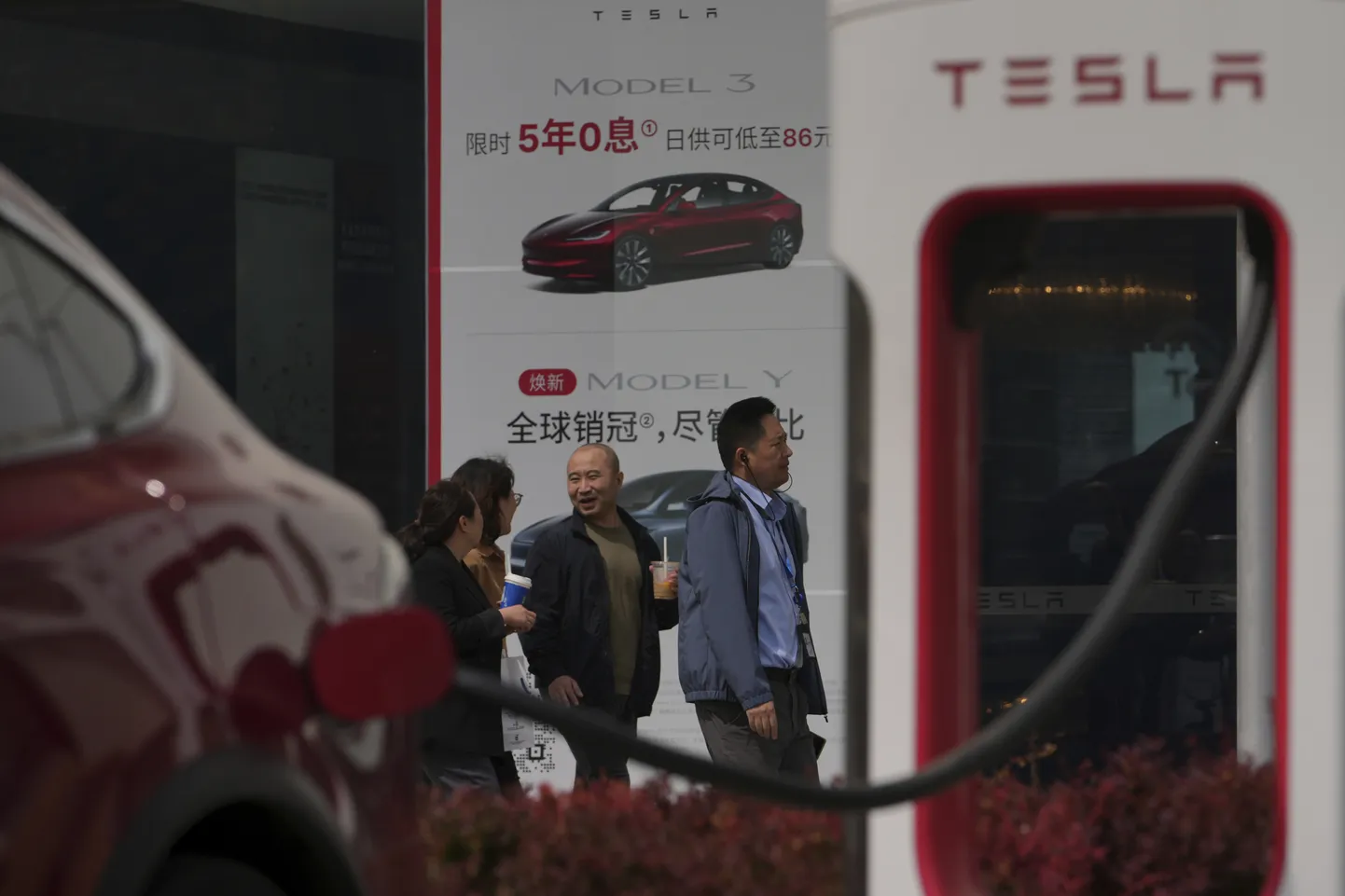 Inimesed kõnnivad mööda sõidukist, mis laeb end elektrisõidukite laadimisjaamas Tesla müügiesinduse ees Pekingis kolmapäeval, 9. aprillil 2025.
