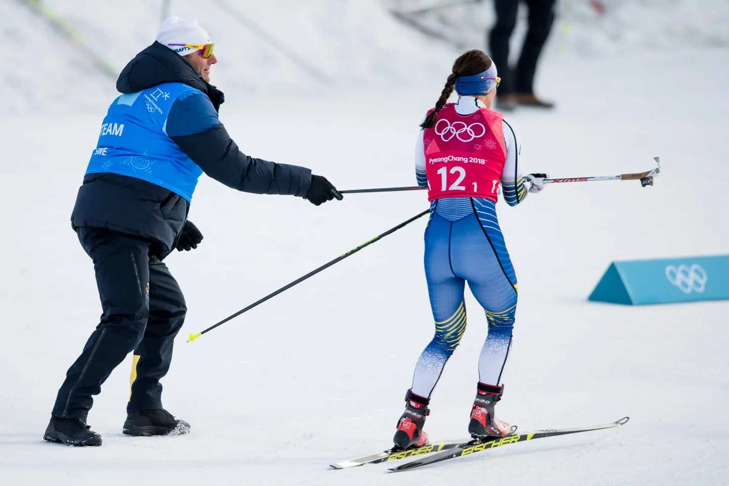 Hooldemees sportlasele suusakeppi ulatamas.