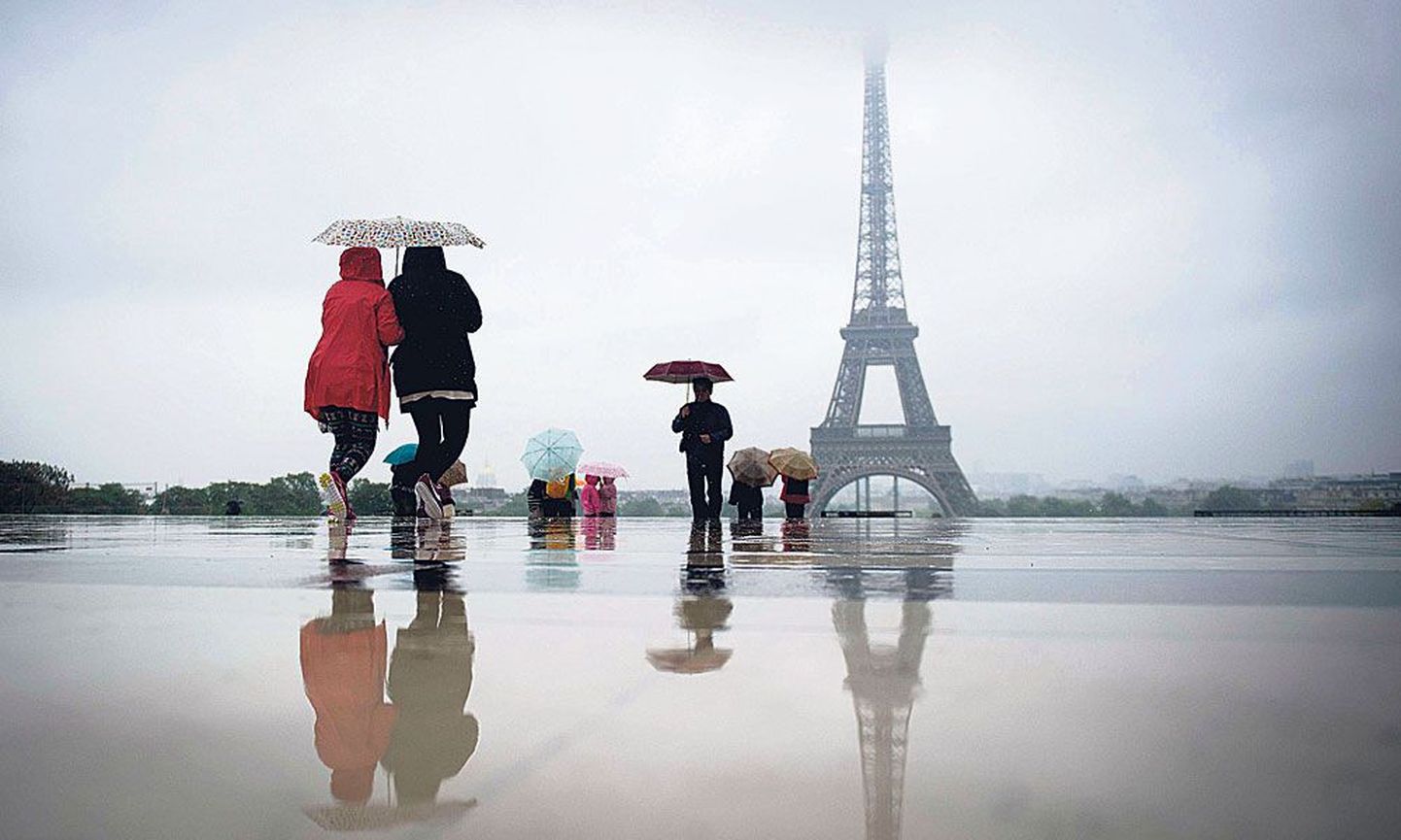 Невзирая на непрекращающийся дождь, туристы идут к Эйфелевой башне.