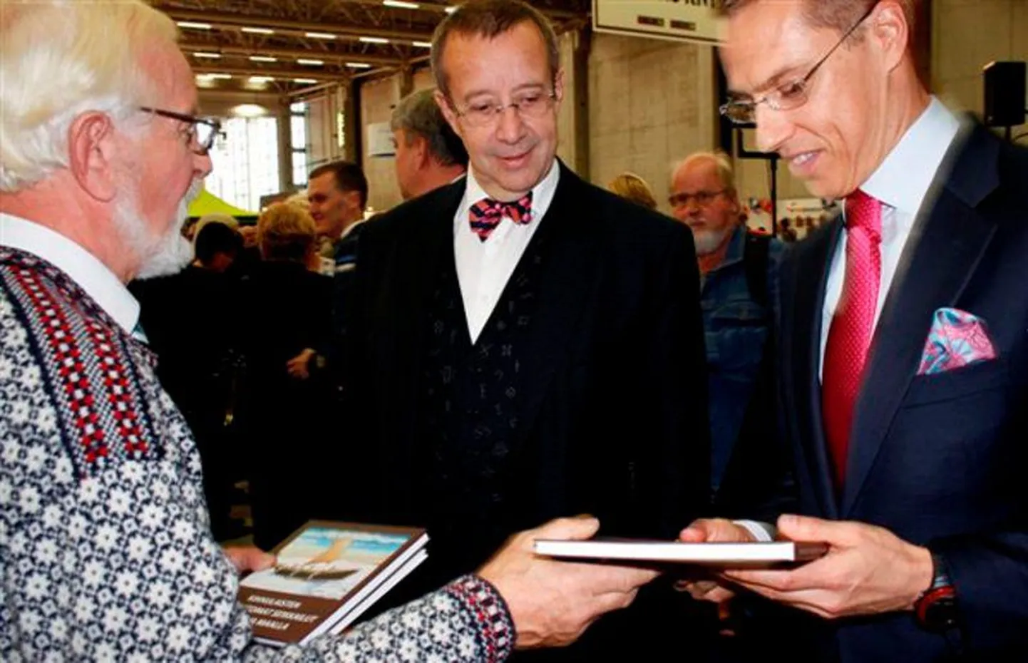 Soome Euroopa ja väliskaubanduse minister Alexander Stubb vaatab üllatunult soomekeelsele kihnlaste uskumatute seikluste kogumikule, mille Kihnu Kultuuri Instituudi nõukogu esimees Mark Soosaar talle president Toomas Hendrik Ilvese juuresolekul üle annab.