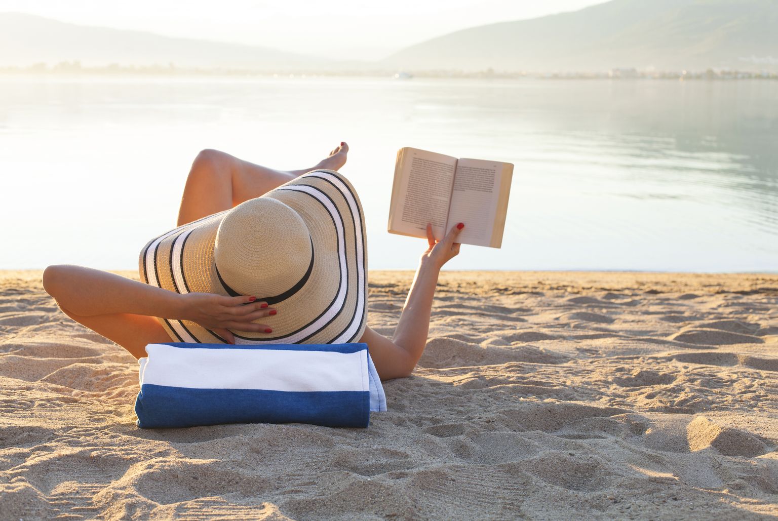 Молодая женщина на пляже читает книгу. Чтение книги в отпуске. Фото иллюстративное.