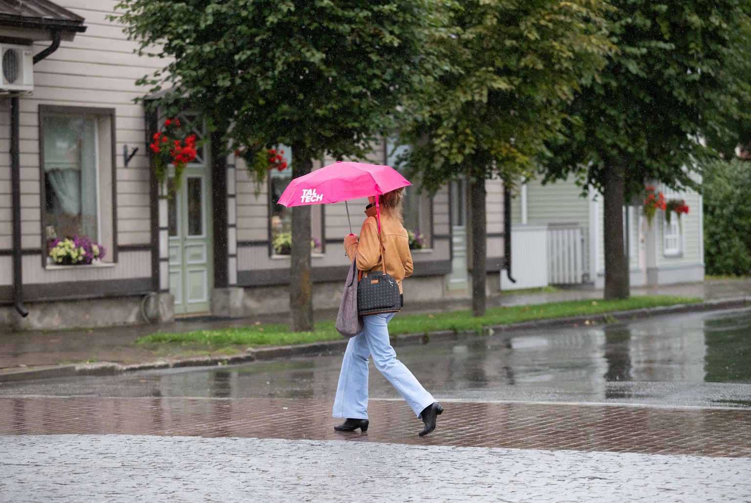 Inimene vihma käes kõndimas, hoides käes vihmavarju.