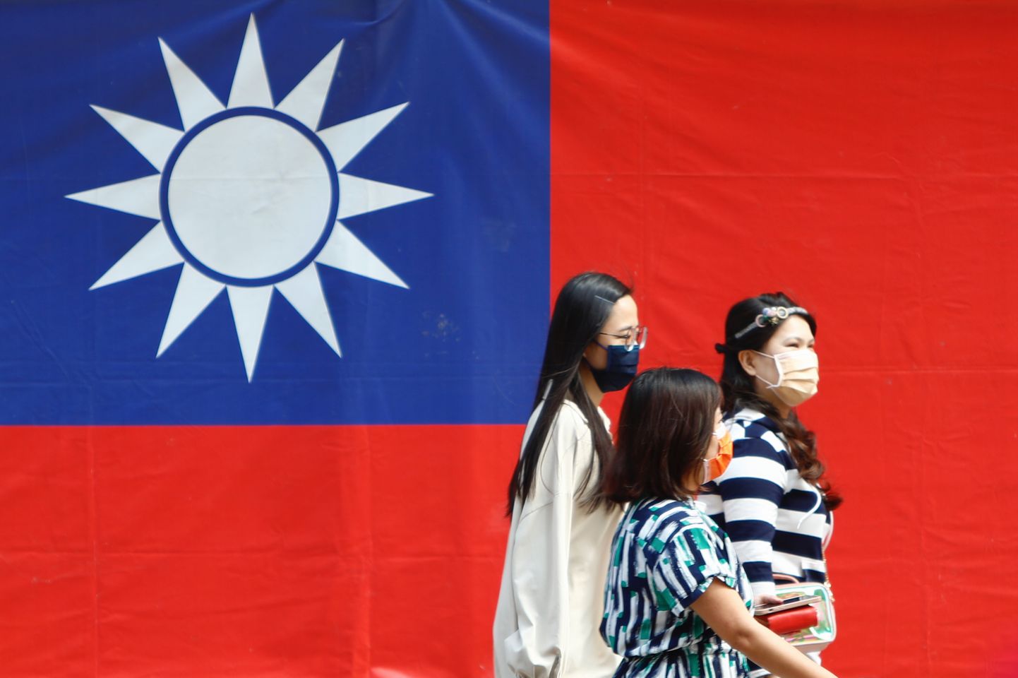 Inimesed kõnnivad Taipei tänaval Taiwani lipu taustal.