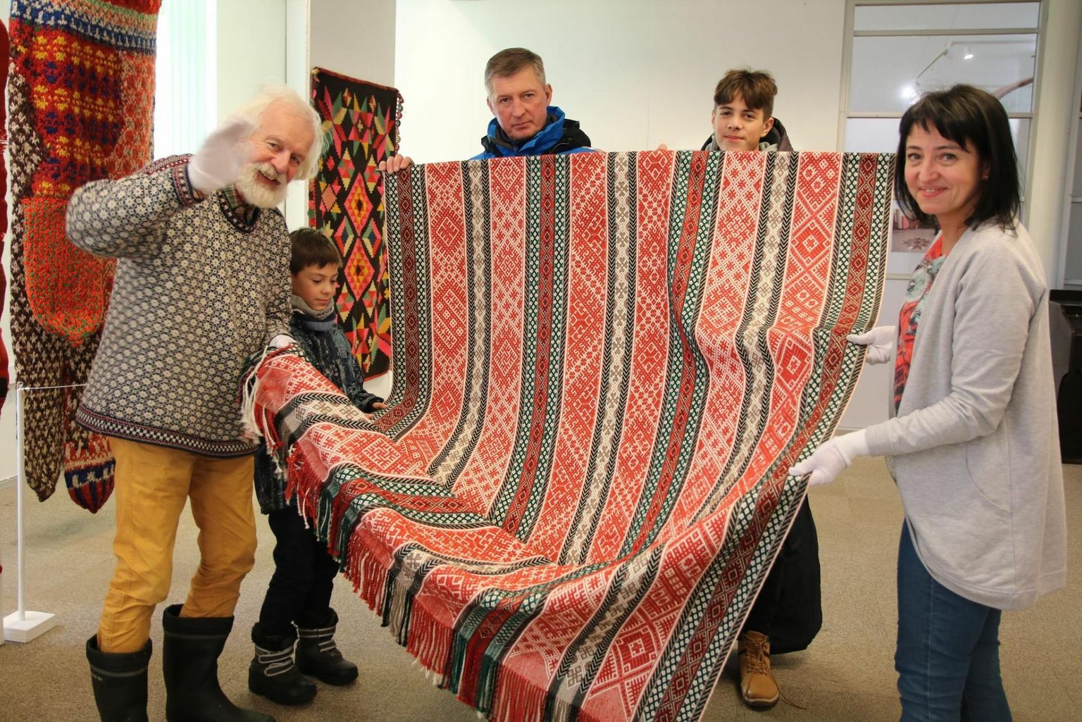Ineta Leja näitab Aluksne rahvakunsti stuudios valminud töid, peakrooni, kätiseid, ristpiste tehnikas patju ja kirivöid. Pildil koos oma pere ja kuraatori Mark Soosaarega.